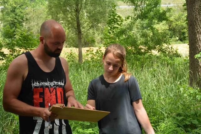 Ein Mann und eine junge Frau stehen im Grünen und schauen gemeinsam auf ein Klemmbrett.