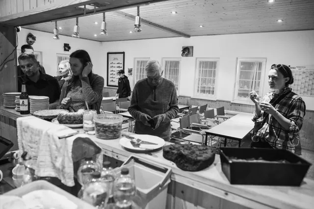 Mehrere Menschen stehen an einer Theke mit verschiedenen Speisen in einem Gemeinschaftsraum.