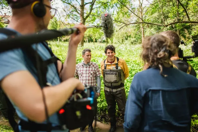 Zwei Männer werden im Grünen von einem Filmteam mit Mikrofon und Kamera gefilmt.