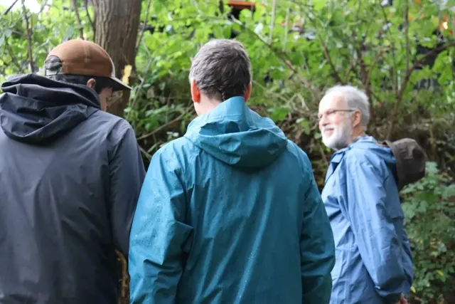 Drei Männer in Outdoor-Kleidung unterhalten sich im Grünen.