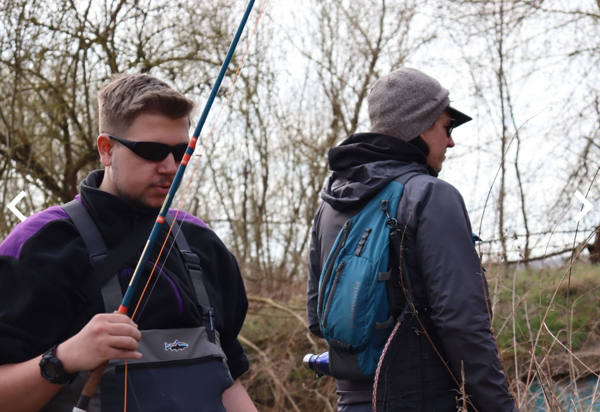 Zwei Personen mit Angelruten stehen am Ufer eines Gewässers und bereiten ihre Ausrüstung vor.
