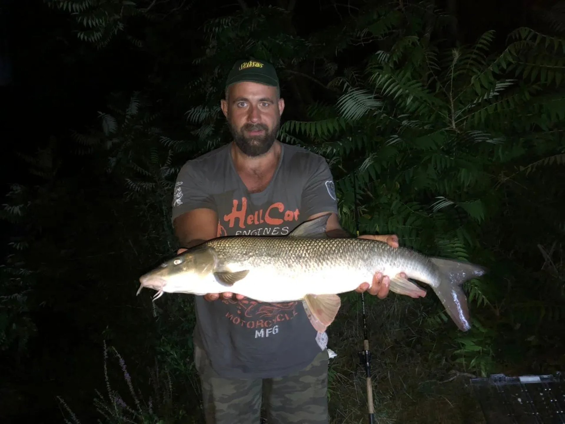 Ein Mann steht im Freien und hält einen großen Fisch mit beiden Händen vor sich.