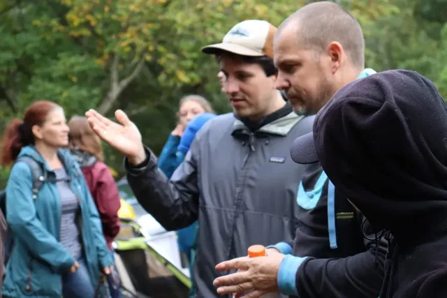 Mehrere Menschen stehen im Freien und unterhalten sich, einige tragen Jacken und Rucksäcke.