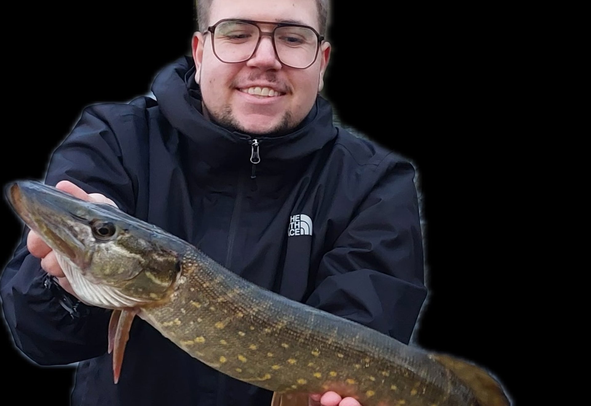 Eine Person hält einen länglichen Hecht mit typischer Punktmusterung vor einem dunklen Hintergrund.