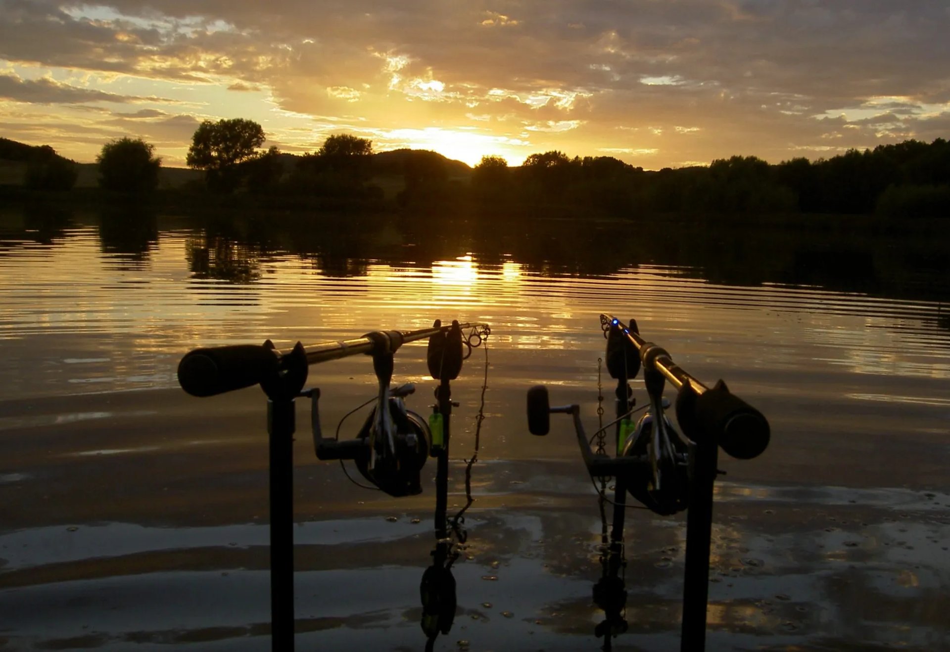 Zwei Angelruten stehen am Ufer eines Sees im Sonnenuntergang.