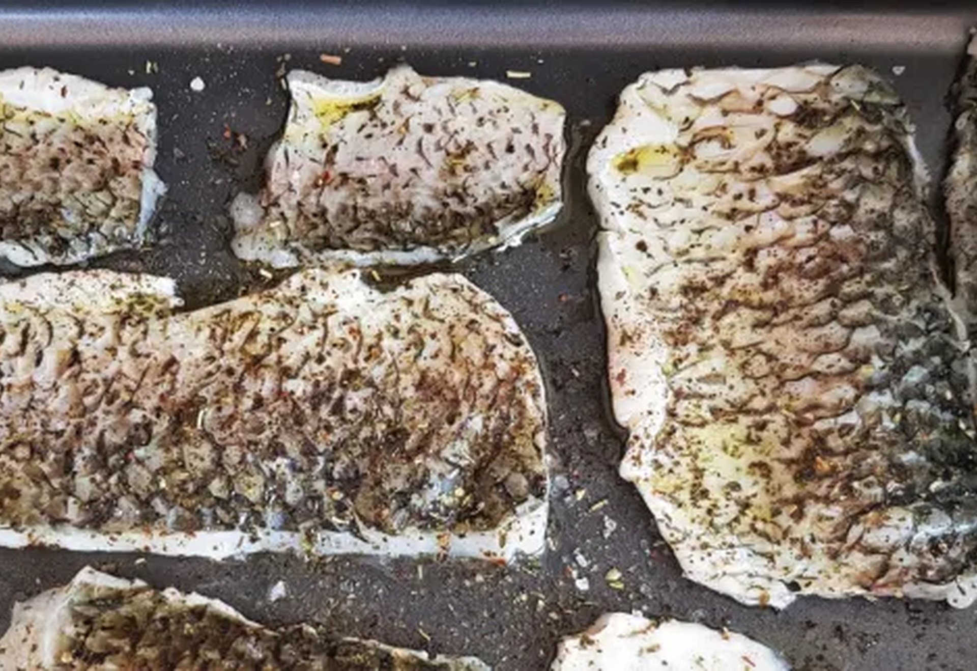 Mehrere gewürzte Fischfilets mit Haut liegen in einem Backblech.