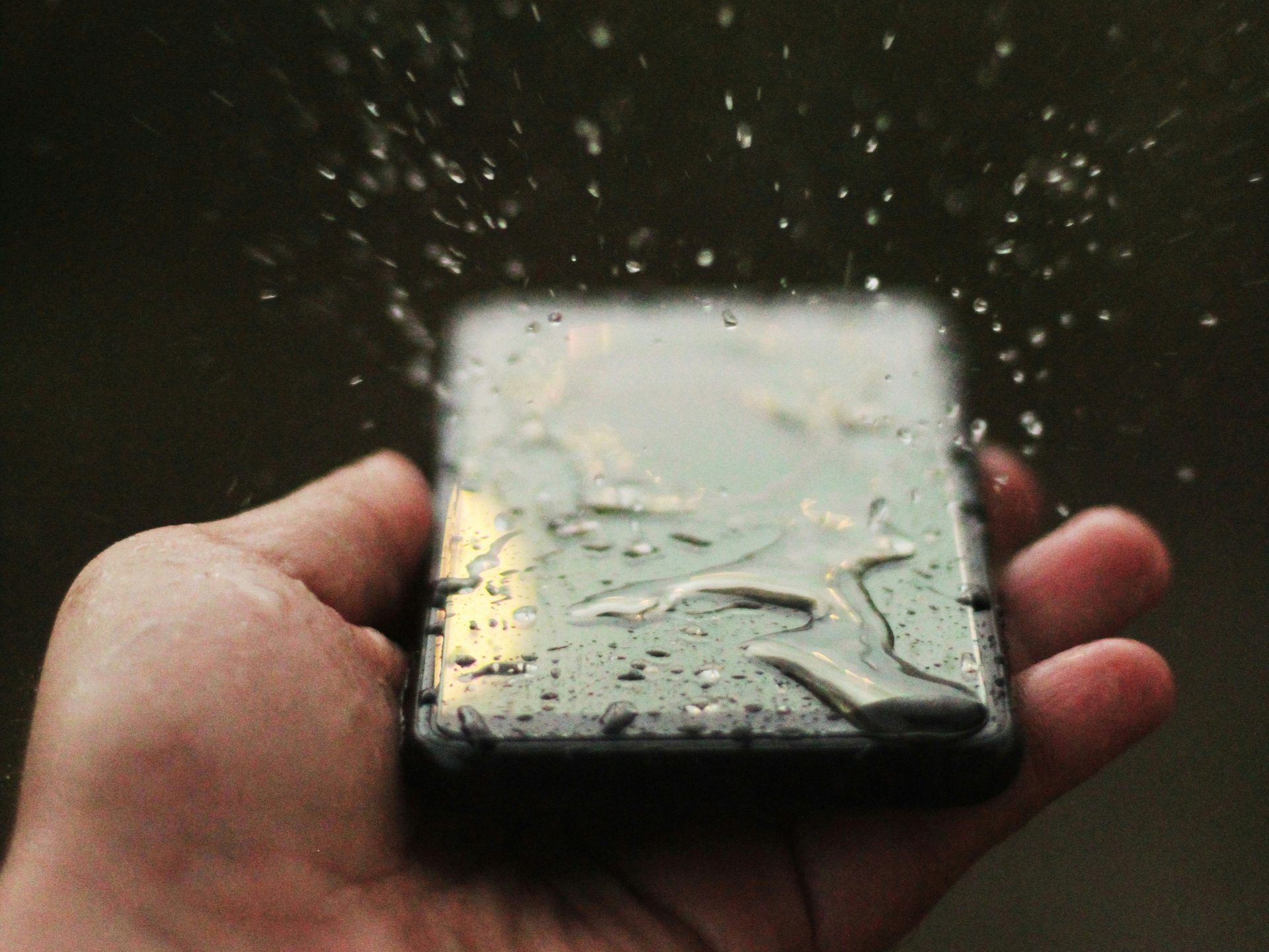 Eine Hand hält ein nasses Smartphone, auf dem Wassertropfen spritzen.