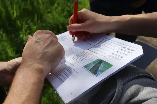 Zwei Personen füllen im Freien gemeinsam einen Fragebogen mit Bildern und Tabellen aus.