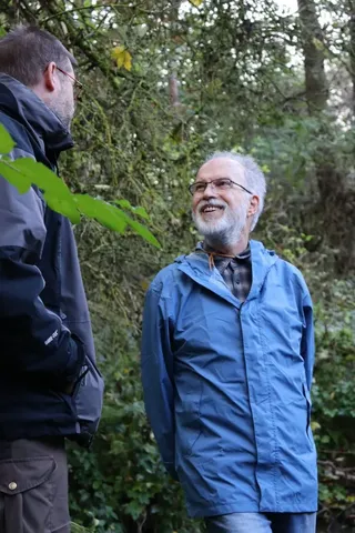 Zwei Männer unterhalten sich lachend im Wald.