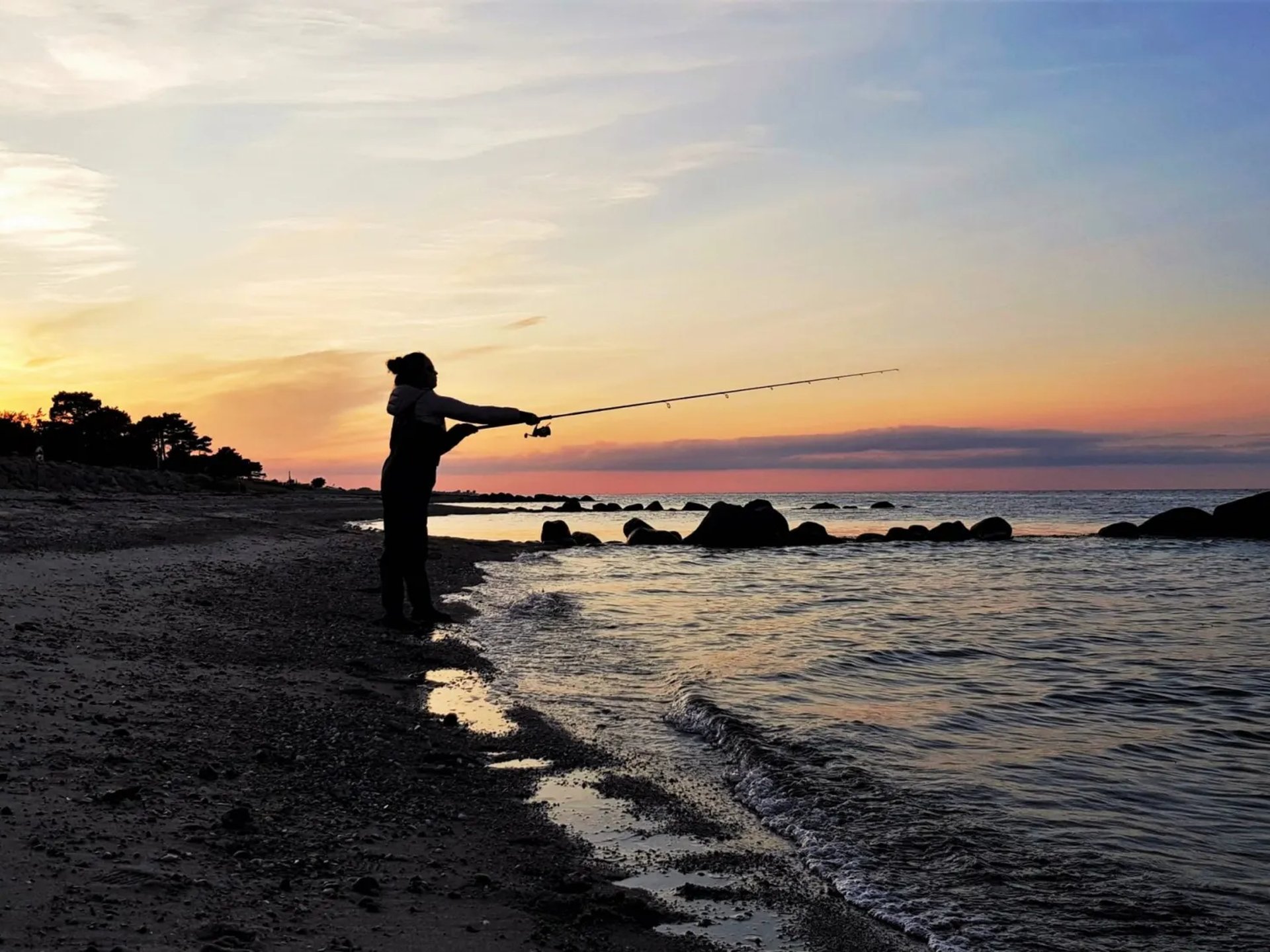 Eine Frau angelt am Ufer bei Sonnenuntergang.