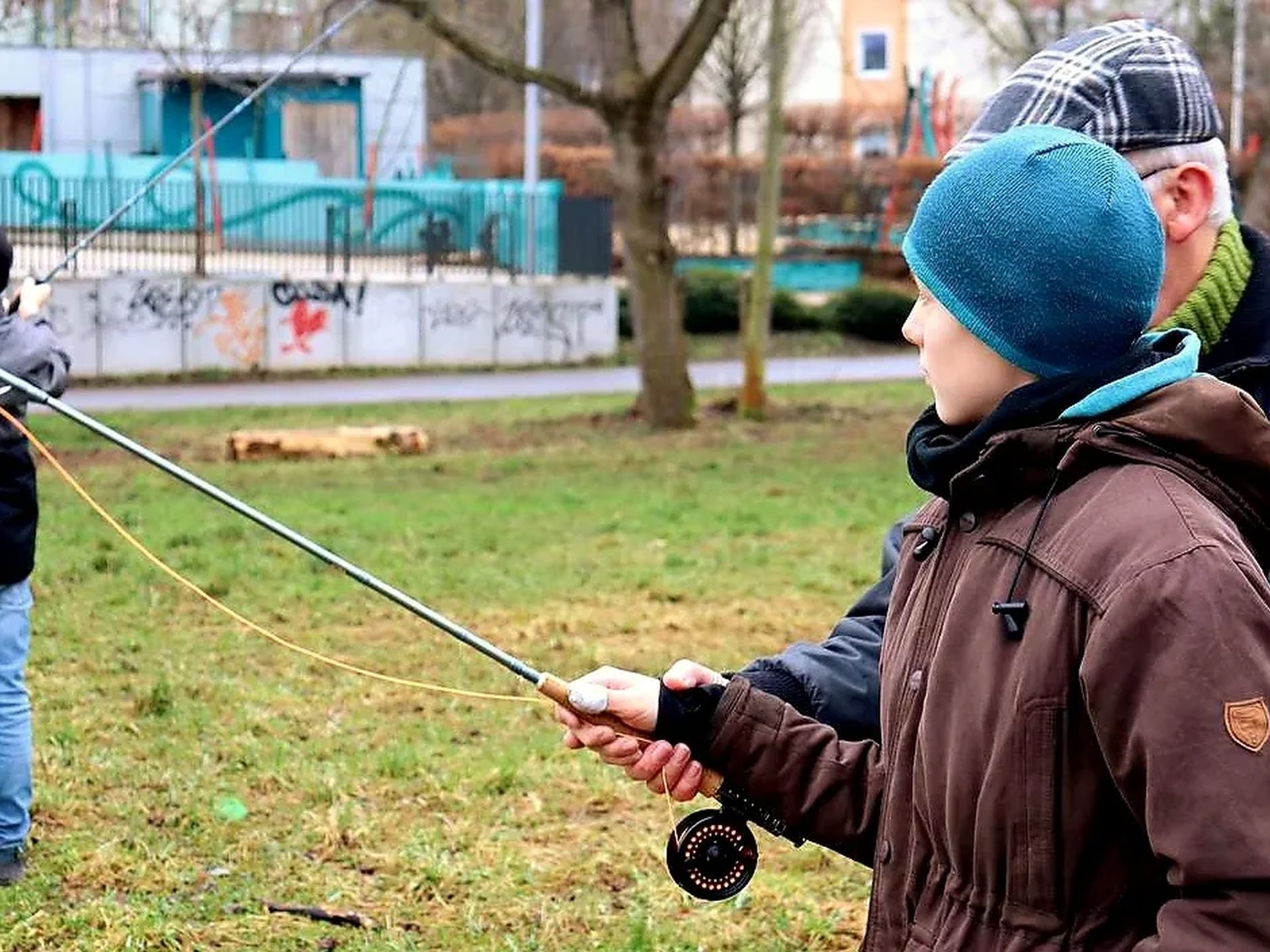 Ein älterer Mann bringt einem Jungen im Freien das Fliegenfischen bei.