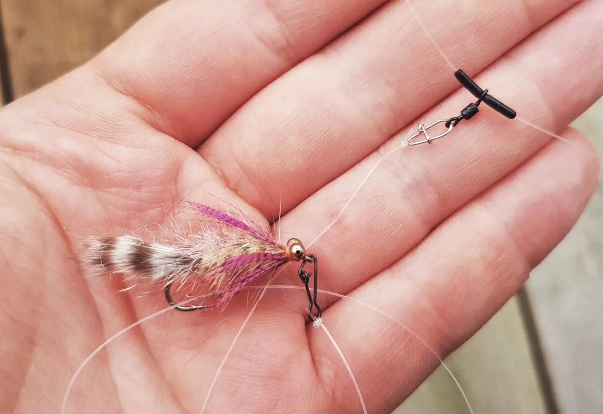 Eine Hand hält eine Angelmontage mit künstlichem Fliegenköder und Vorfach.