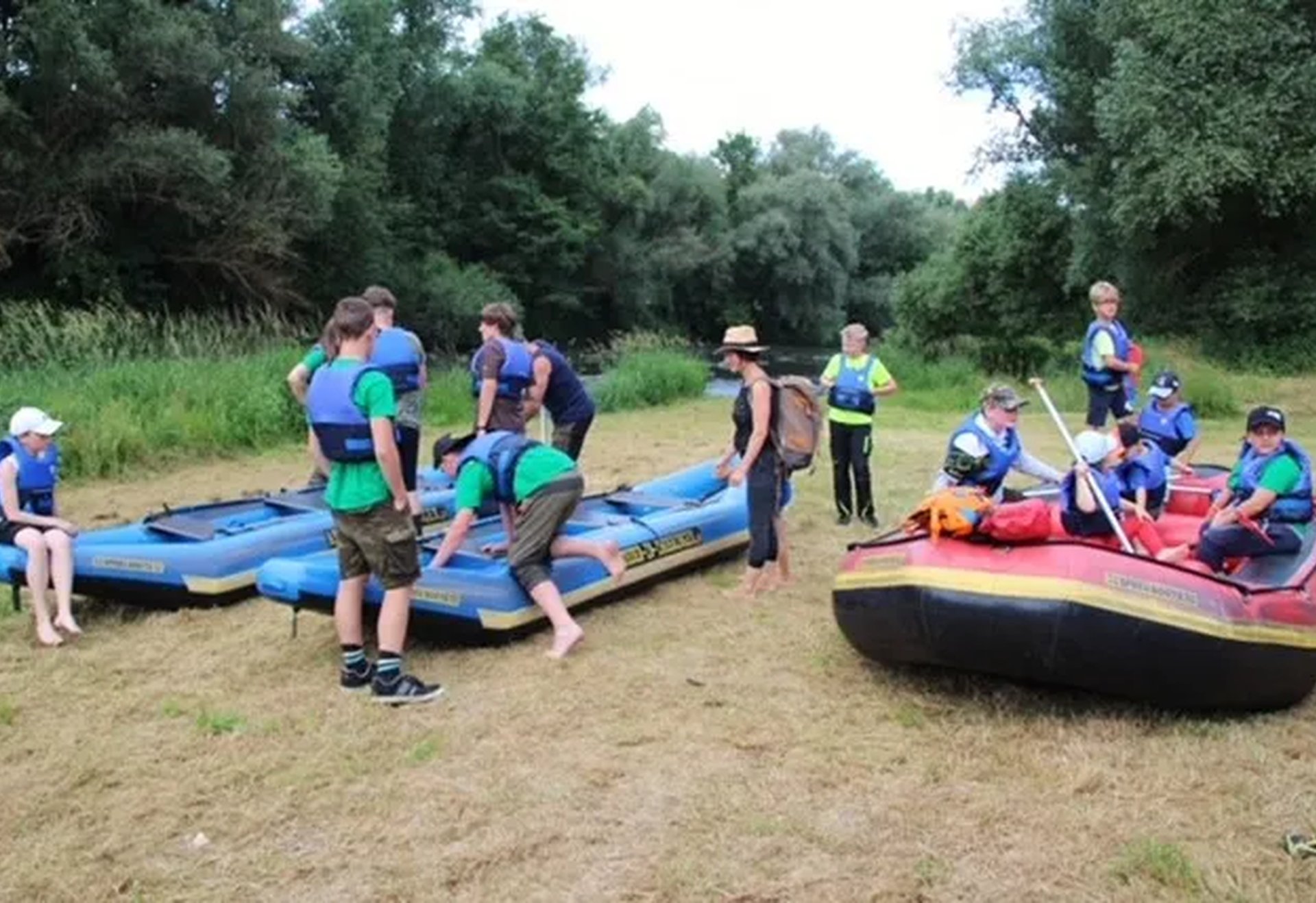 Mehrere Kinder und Erwachsene mit Schwimmwesten bereiten sich am Ufer mit Schlauchbooten auf eine Fahrt vor.