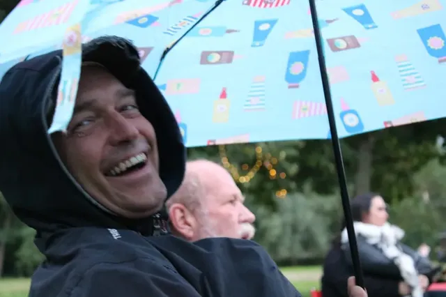 Ein lachender Mann sitzt im Freien unter einem bunten Regenschirm.