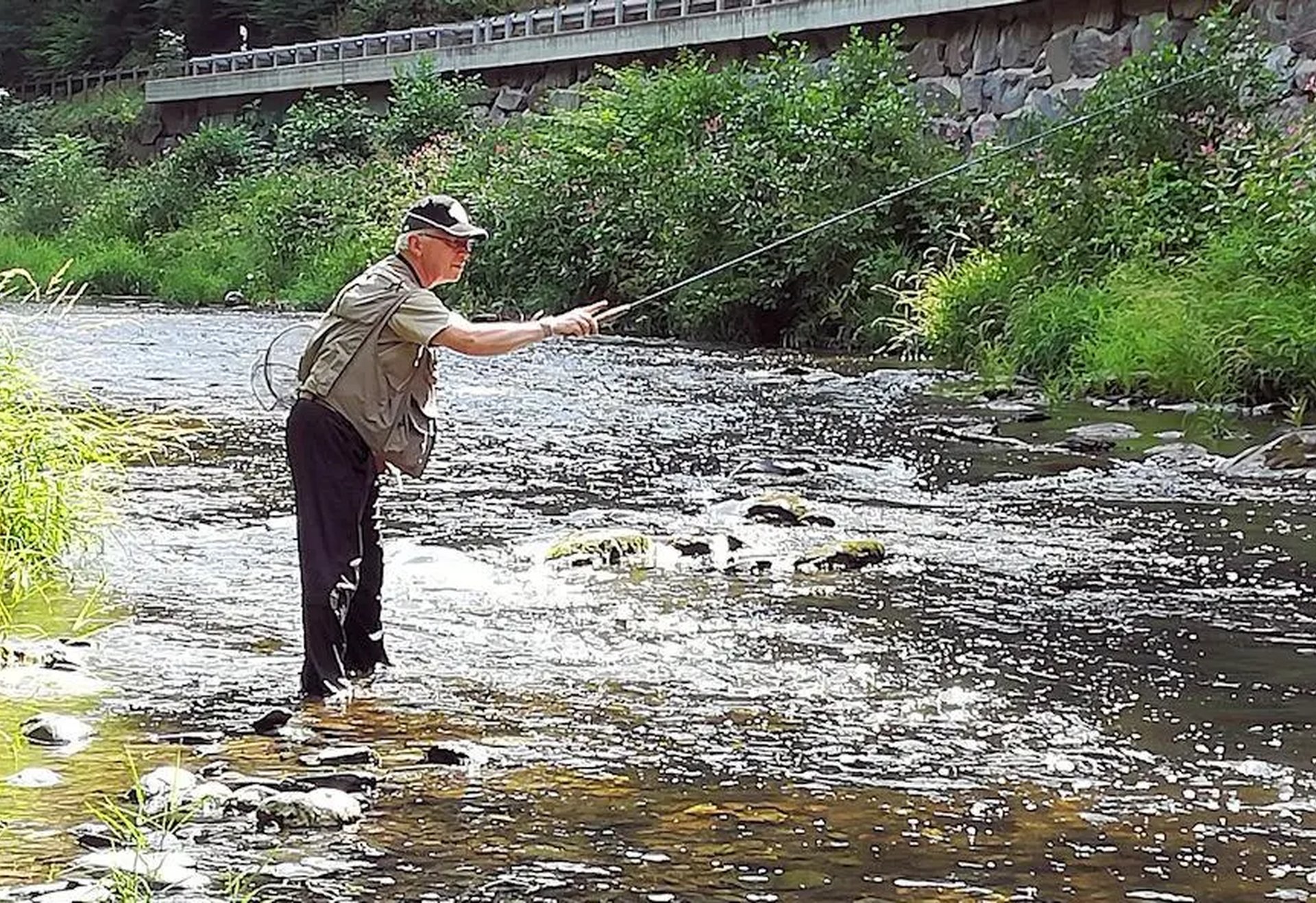 Ein Mann steht in einem Bach und angelt mit einer Fliegenrute.