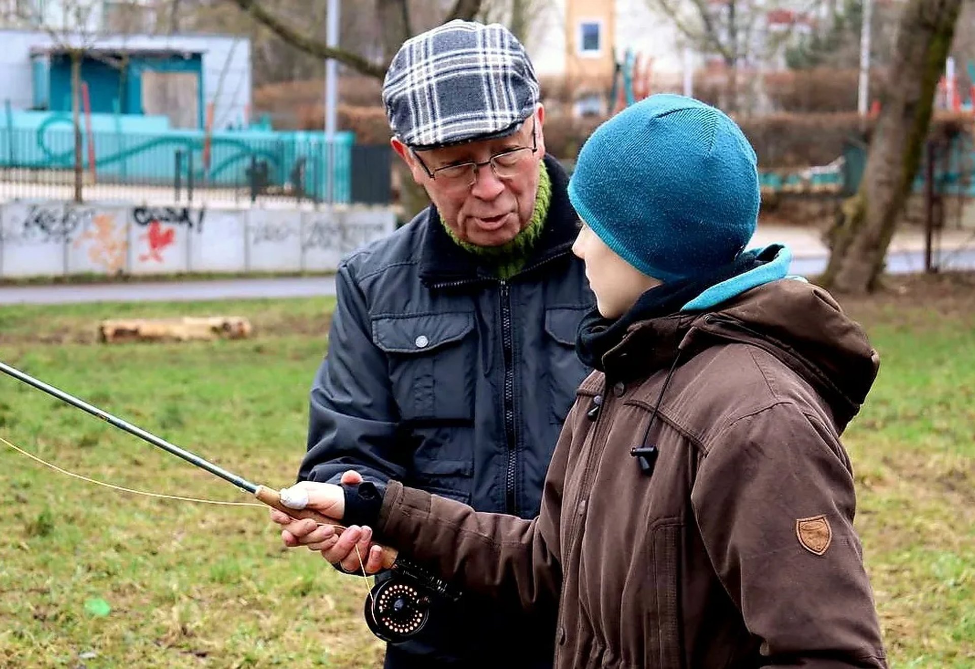 Ein älterer Mann zeigt einem Jungen im Freien, wie man eine Angelrute hält.