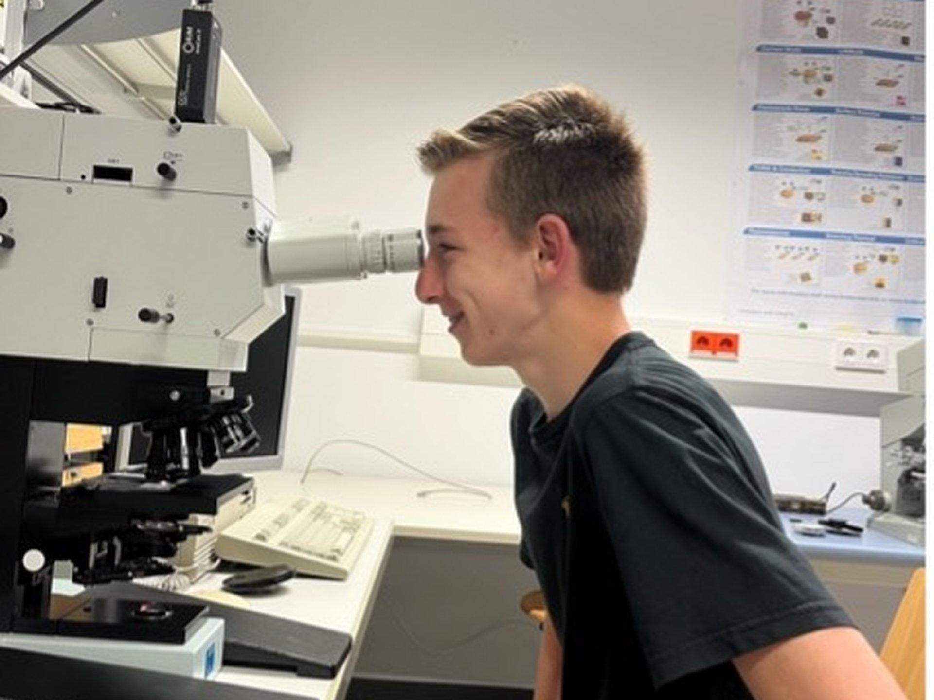 Ein junger Mann sitzt an einem Mikroskop und schaut hindurch.