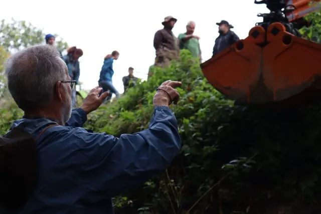 Ein Mann weist eine Gruppe von Menschen und einen Bagger an einem Hang an.