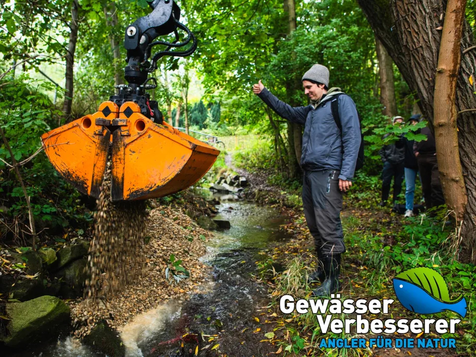 Ein Bagger schüttet Kies in einen kleinen Bach, während ein Mann daneben steht und zuschaut; im Vordergrund ist das Logo „Gewässer-Verbesserer – Angler für die Natur“.
