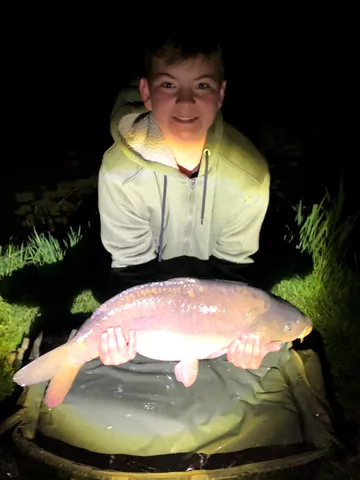 Ein Jugendlicher hält nachts einen großen Fisch und lächelt in die Kamera.