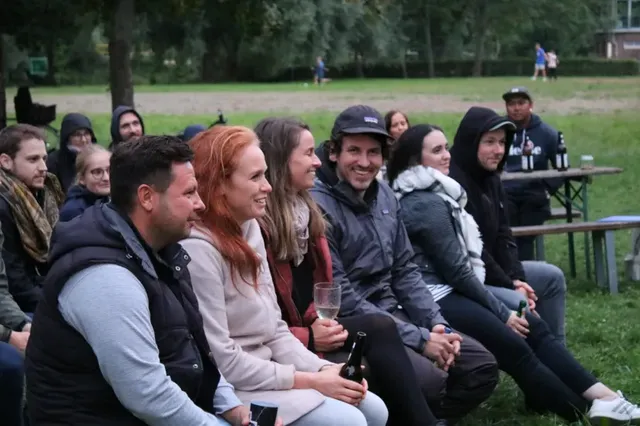 Mehrere Menschen sitzen im Freien auf Bänken und schauen lächelnd nach vorne.