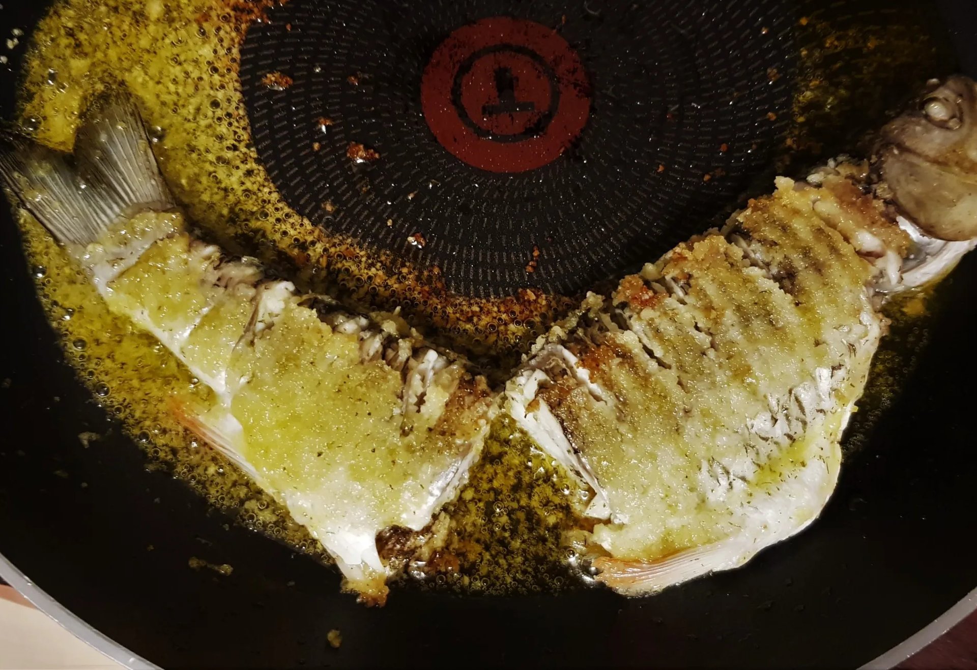 Ein ganzer Fisch wird in einer Pfanne mit Öl angebraten.