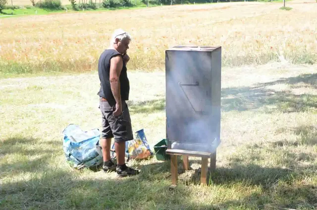 Ein Mann steht im Freien neben einem rauchenden Metallkasten auf Beinen.