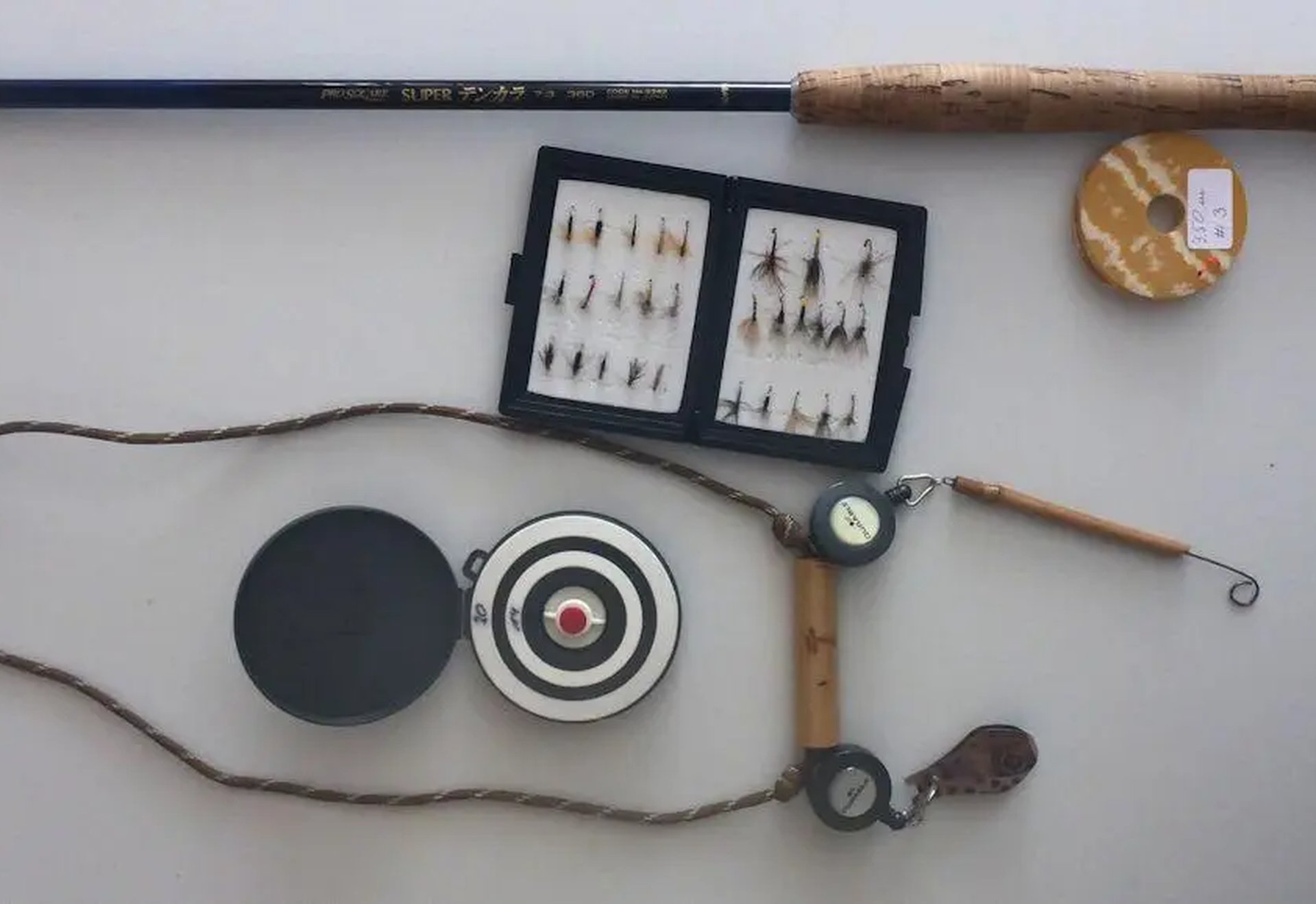 Angelzubehör bestehend aus einer Angelrute, einer Dose mit Angelschnur, einer Dose mit künstlichen Fliegen, einem Maßband, einer Zielscheibe und weiterem Angelwerkzeug.