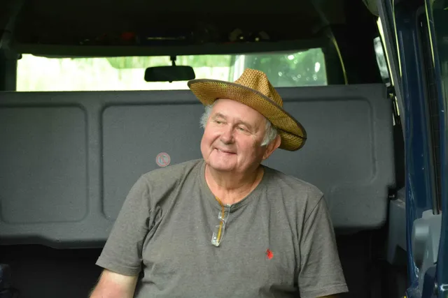 Ein älterer Mann mit Strohhut sitzt lächelnd in einem Auto.