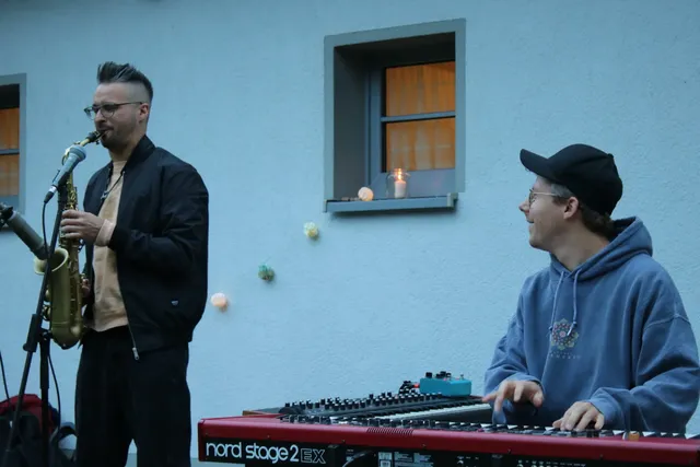 Zwei Musiker spielen im Freien; einer spielt Saxophon, der andere sitzt am Keyboard.
