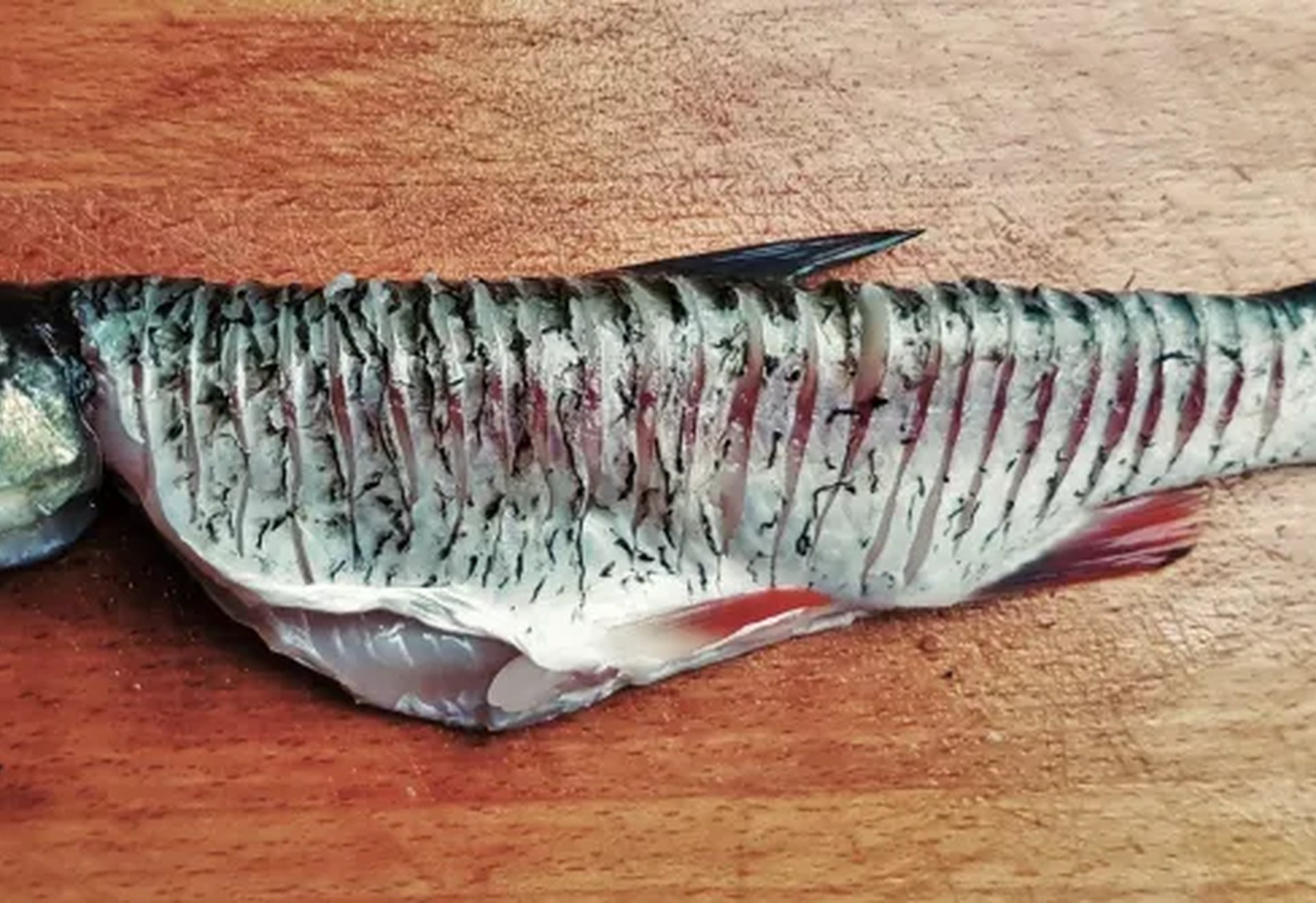 Ein aufgeschnittener Fisch liegt auf einem Holzbrett.