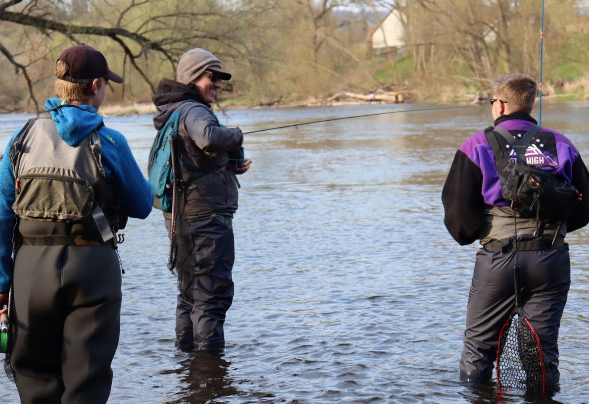 Drei Personen stehen im hüfttiefen Wasser eines Flusses und angeln gemeinsam.