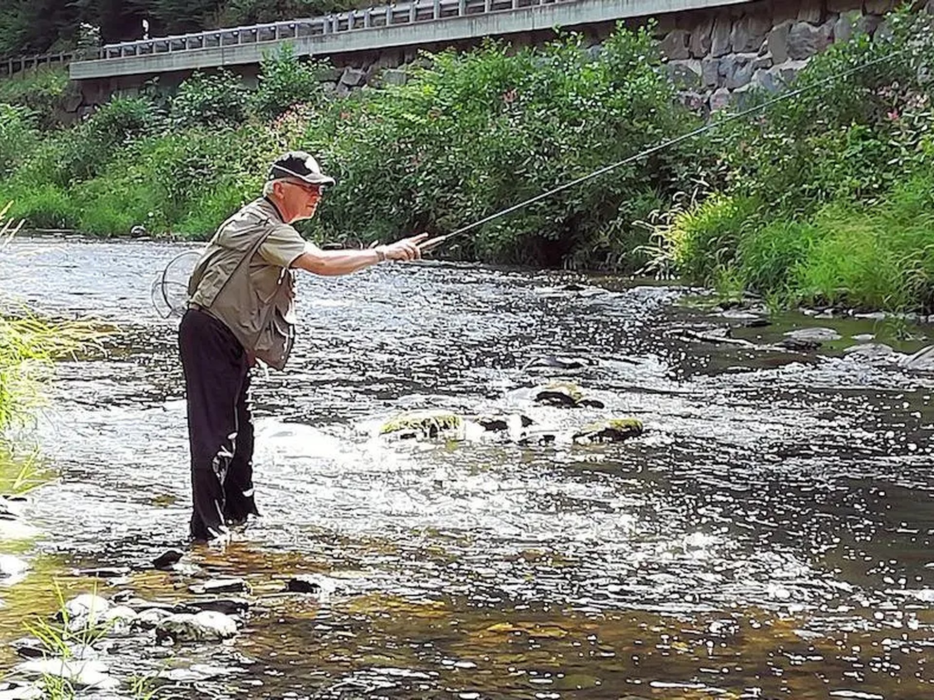 Ein Mann steht in einem Fluss und angelt mit einer Angelrute.