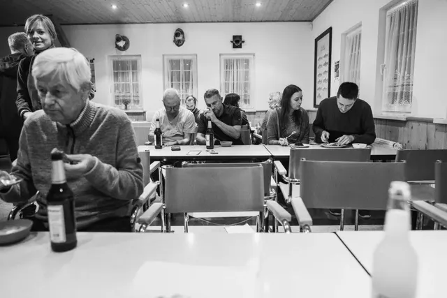 Mehrere Menschen sitzen in einem Raum an Tischen, essen und trinken; die Stimmung wirkt ruhig und entspannt.