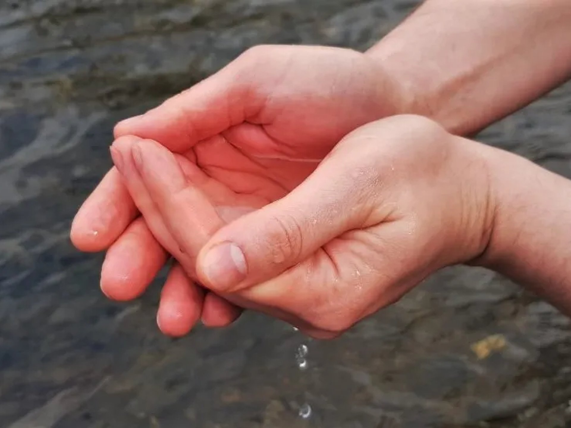 Zwei Hände formen eine Schale und halten Wasser über einem Fluss oder See.
