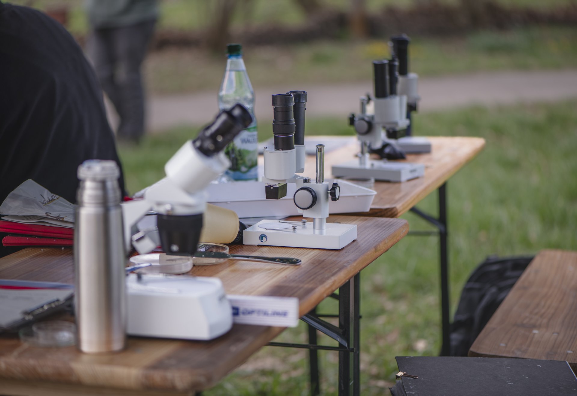Drei Stereolupen stehen auf einem Holztisch im Freien, daneben befinden sich weitere Utensilien.