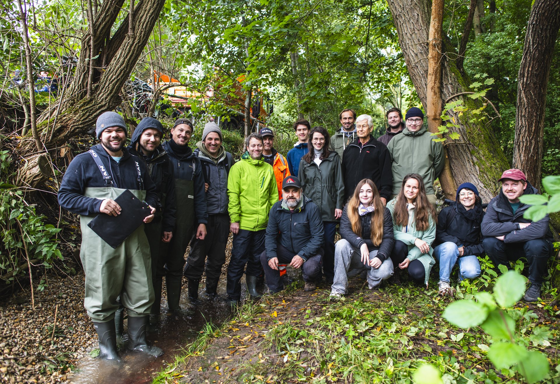 Eine Gruppe von Menschen steht und sitzt im Grünen unter Bäumen und lächelt in die Kamera.