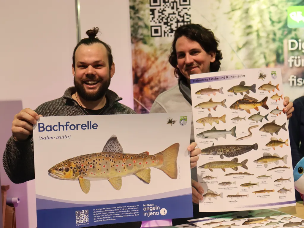 Zwei Männer halten Poster mit Fischabbildungen, einer davon zeigt eine Bachforelle.