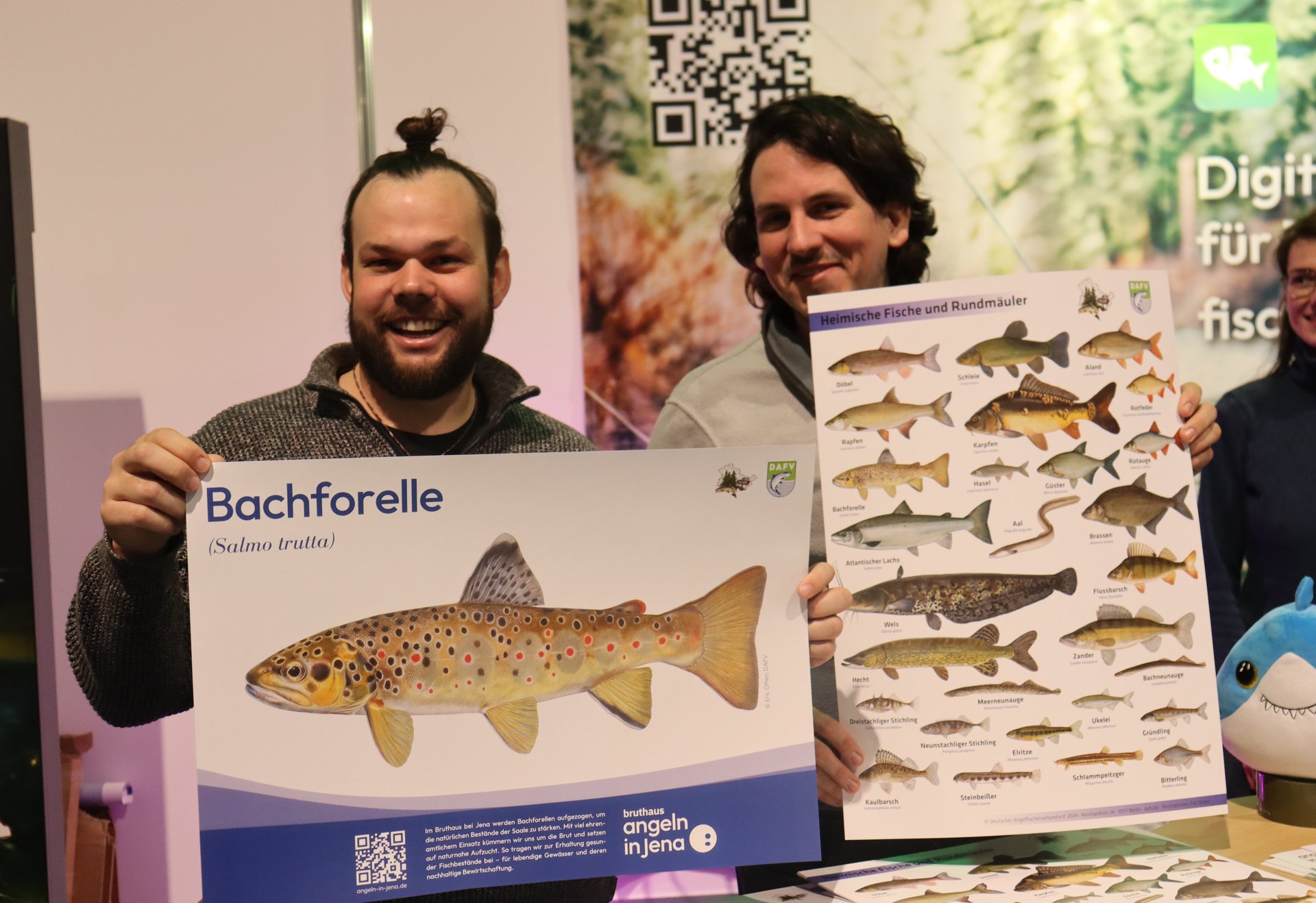 Zwei Männer halten Poster mit Fischabbildungen, einer davon zeigt eine Bachforelle.