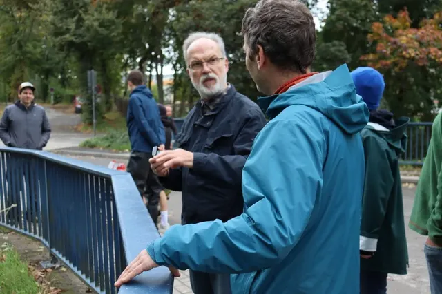 Mehrere Menschen stehen im Freien an einem blauen Geländer und unterhalten sich.